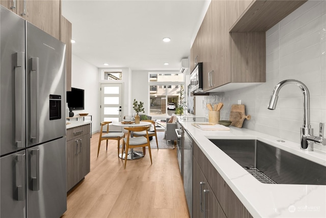 kitchen with sink, light hardwood / wood-style flooring, stainless steel appliances, tasteful backsplash, and light stone counters