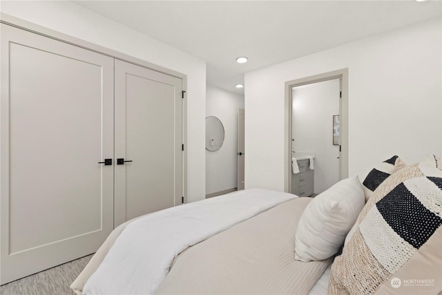 bedroom with ensuite bathroom, light hardwood / wood-style flooring, and a closet