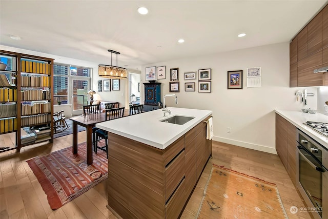 kitchen with sink, light hardwood / wood-style flooring, hanging light fixtures, and appliances with stainless steel finishes