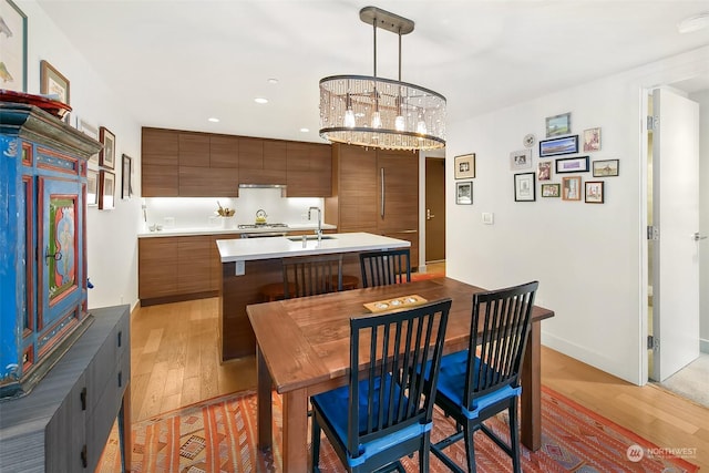 kitchen with sink, hardwood / wood-style flooring, hanging light fixtures, gas stovetop, and a center island with sink