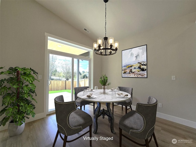 dining space with hardwood / wood-style flooring, vaulted ceiling, and an inviting chandelier