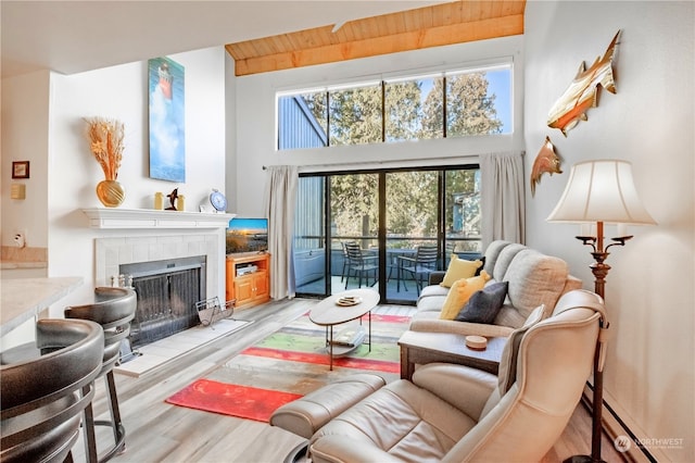 sitting room with wood ceiling, light hardwood / wood-style flooring, a towering ceiling, a tiled fireplace, and a baseboard radiator