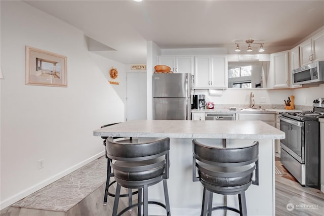 kitchen with white cabinetry, sink, stainless steel appliances, and a kitchen bar