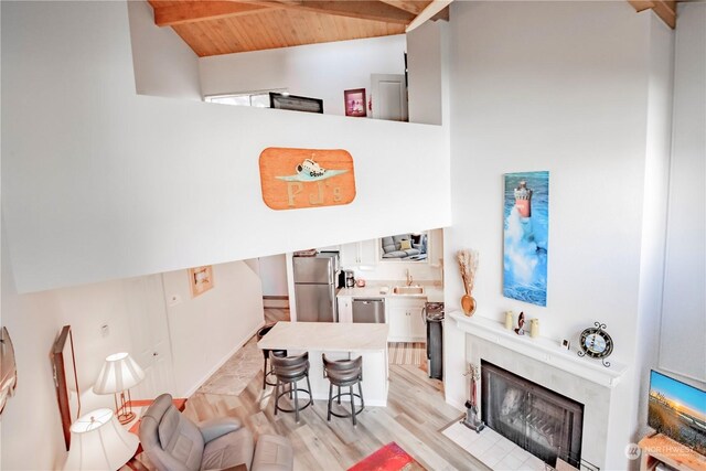 living room with sink, a premium fireplace, vaulted ceiling with beams, light hardwood / wood-style floors, and wooden ceiling