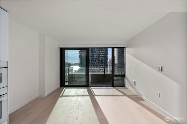 spare room with floor to ceiling windows and light hardwood / wood-style flooring