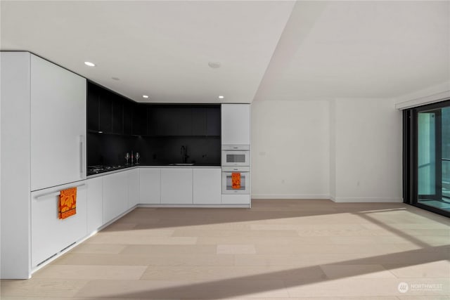 kitchen with white cabinetry, sink, double oven, and light hardwood / wood-style flooring