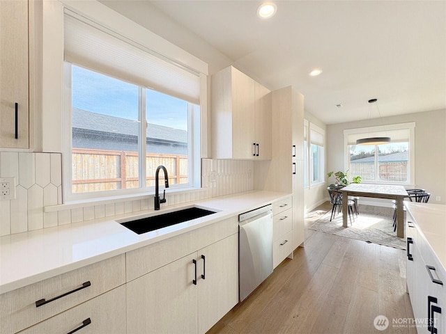 kitchen with sink, dishwasher, decorative light fixtures, light hardwood / wood-style floors, and decorative backsplash