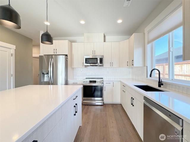 kitchen featuring hardwood / wood-style floors, appliances with stainless steel finishes, sink, backsplash, and decorative light fixtures