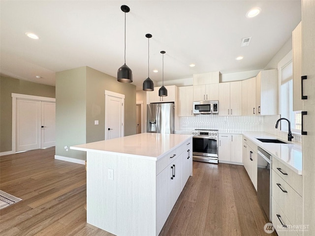 kitchen featuring appliances with stainless steel finishes, hanging light fixtures, decorative backsplash, a kitchen island, and sink