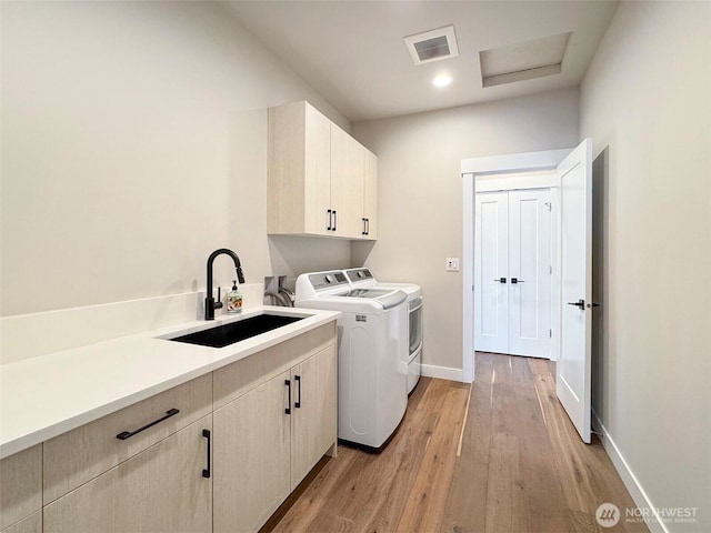 laundry area featuring sink, cabinets, washing machine and clothes dryer, and light hardwood / wood-style floors