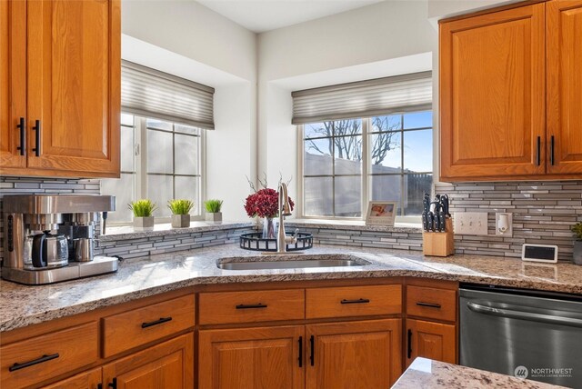 kitchen featuring tasteful backsplash, dishwasher, sink, and light stone countertops