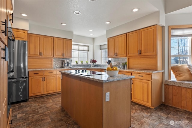 kitchen featuring light stone counters, stainless steel fridge, a kitchen island, black electric stovetop, and decorative backsplash