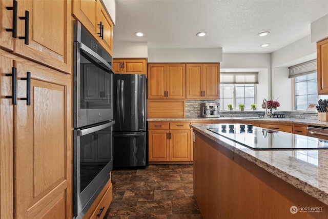 kitchen with sink, backsplash, light stone countertops, black appliances, and a textured ceiling