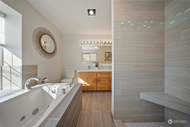 bathroom with vanity, tiled bath, and toilet