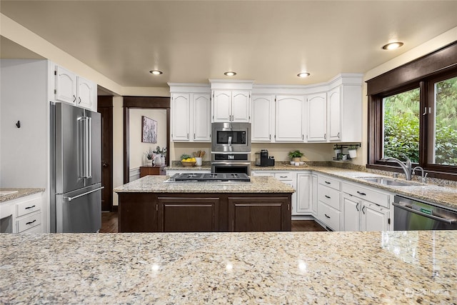 kitchen with sink, appliances with stainless steel finishes, white cabinetry, a center island, and light stone countertops