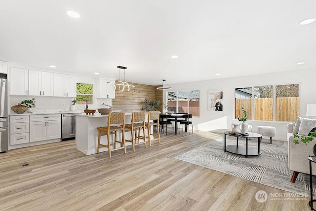 kitchen featuring light hardwood / wood-style floors, appliances with stainless steel finishes, white cabinetry, decorative light fixtures, and a kitchen island