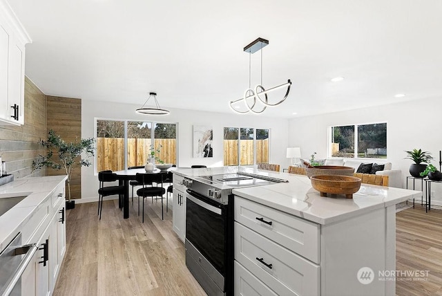 kitchen with light stone countertops, white cabinets, a kitchen island, decorative light fixtures, and stainless steel appliances