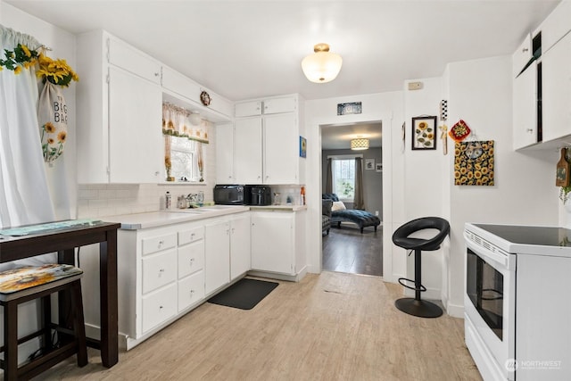 kitchen featuring white range with electric cooktop, light hardwood / wood-style flooring, sink, white cabinets, and decorative backsplash