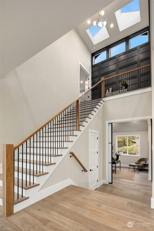 staircase with a towering ceiling, a skylight, and hardwood / wood-style floors