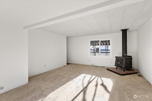 unfurnished living room with a wood stove, light colored carpet, and beamed ceiling