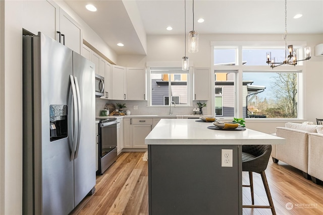 kitchen featuring stainless steel appliances, a kitchen bar, decorative light fixtures, and white cabinets