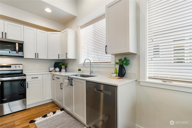 kitchen featuring stainless steel appliances, white cabinetry, sink, and light hardwood / wood-style flooring