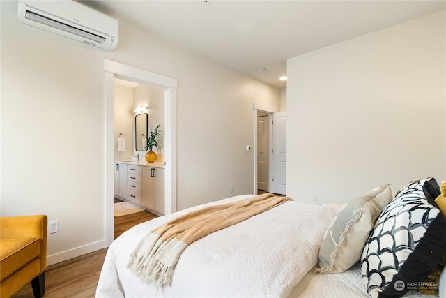 bedroom with a wall mounted air conditioner, connected bathroom, and light hardwood / wood-style flooring