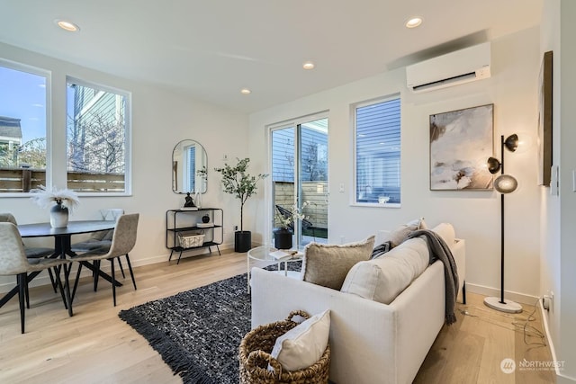 living area with recessed lighting, light wood-style flooring, an AC wall unit, and baseboards