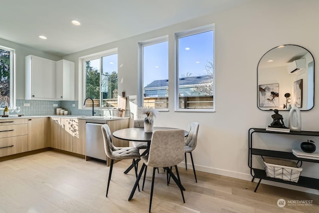 kitchen with light brown cabinets, light hardwood / wood-style flooring, dishwasher, an AC wall unit, and decorative backsplash