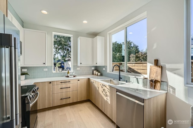 kitchen with appliances with stainless steel finishes, light brown cabinets, sink, backsplash, and light hardwood / wood-style flooring