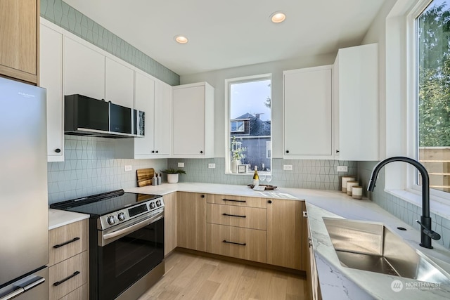 kitchen with white cabinets, stainless steel appliances, light hardwood / wood-style floors, sink, and backsplash