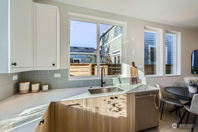 kitchen with light stone counters, white cabinetry, a sink, decorative backsplash, and stainless steel dishwasher