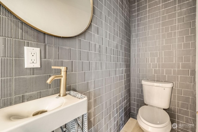 bathroom featuring tile walls, toilet, and a sink