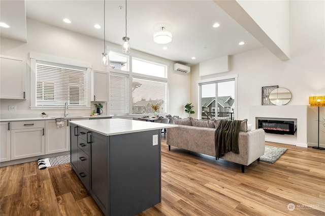 kitchen with a wall unit AC, a center island, light hardwood / wood-style floors, white cabinets, and decorative light fixtures