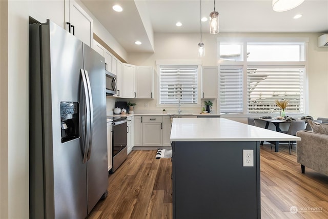 kitchen with white cabinetry, decorative light fixtures, a center island, appliances with stainless steel finishes, and hardwood / wood-style floors