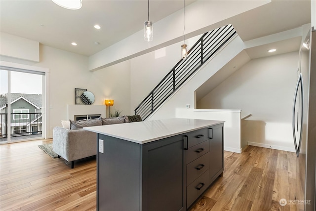 kitchen featuring stainless steel refrigerator, a center island, light wood-type flooring, and decorative light fixtures