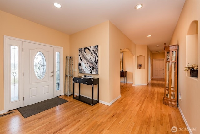 foyer with arched walkways, light wood-style flooring, recessed lighting, visible vents, and baseboards