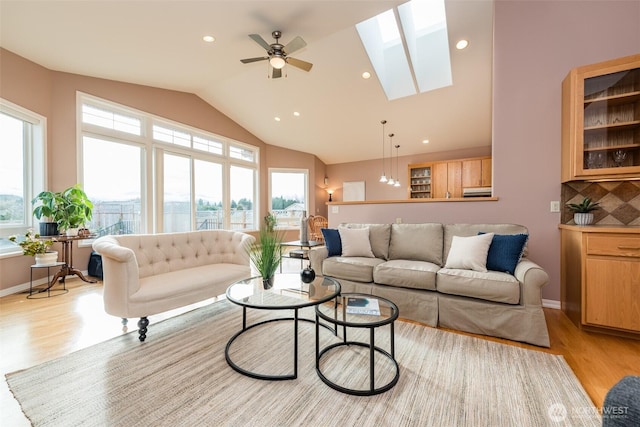 living room featuring lofted ceiling with skylight, recessed lighting, light wood finished floors, and a ceiling fan