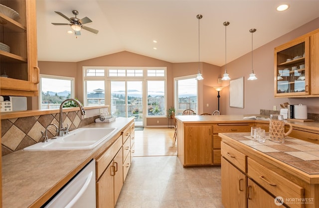 kitchen with pendant lighting, light countertops, glass insert cabinets, a sink, and dishwashing machine