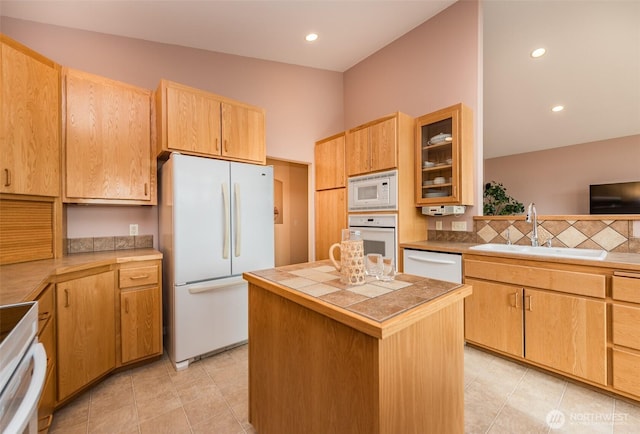 kitchen featuring light brown cabinets, white appliances, a sink, a center island, and glass insert cabinets