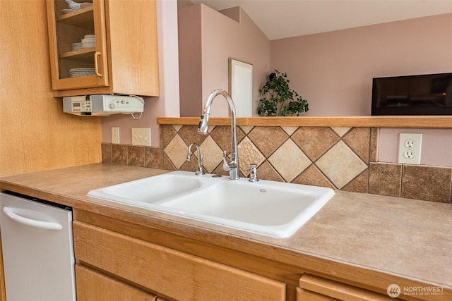 kitchen featuring a sink, light countertops, stainless steel dishwasher, backsplash, and glass insert cabinets