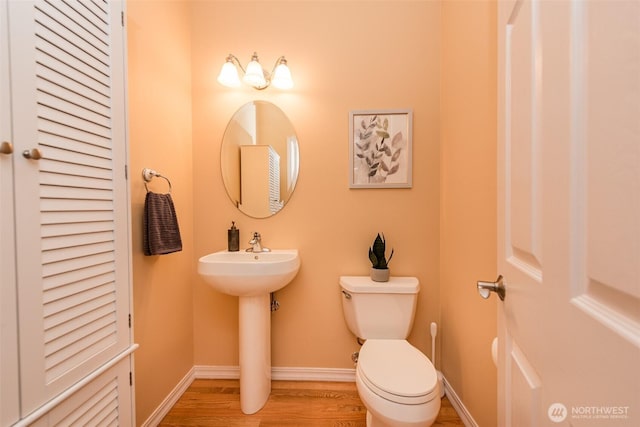 bathroom featuring a closet, toilet, a sink, wood finished floors, and baseboards