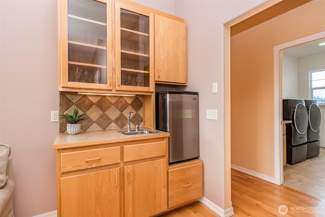 kitchen with tasteful backsplash, glass insert cabinets, washing machine and clothes dryer, light countertops, and a sink