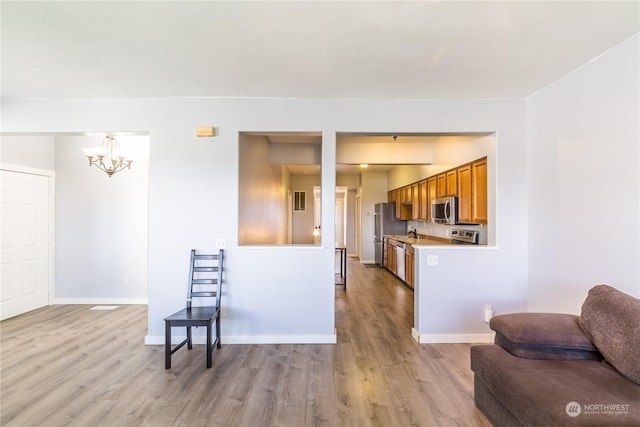 kitchen with open floor plan, appliances with stainless steel finishes, brown cabinetry, and light wood-type flooring