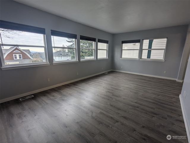 spare room with dark wood-style flooring, visible vents, and baseboards