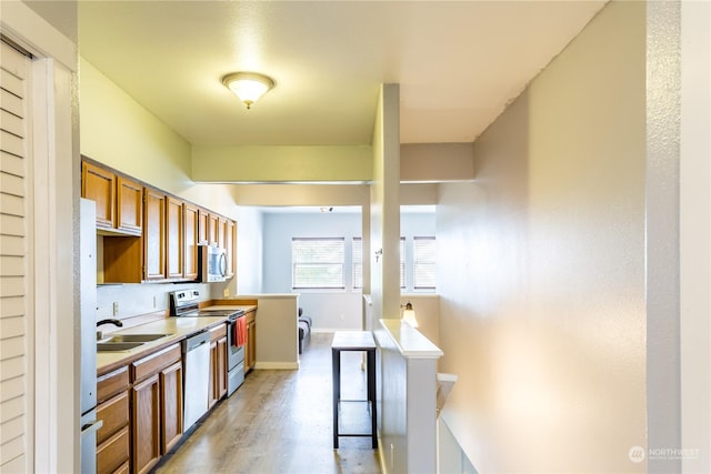 kitchen with a sink, light countertops, appliances with stainless steel finishes, light wood-type flooring, and brown cabinetry