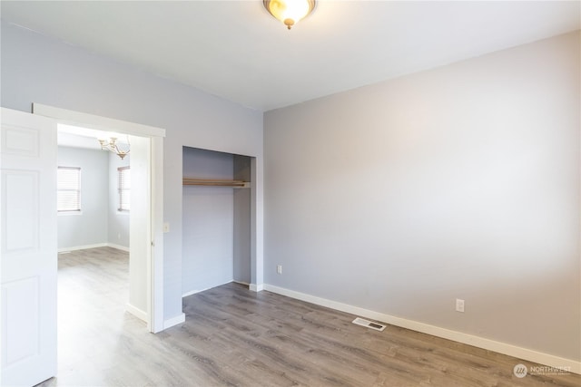 unfurnished bedroom featuring hardwood / wood-style flooring, a chandelier, and a closet