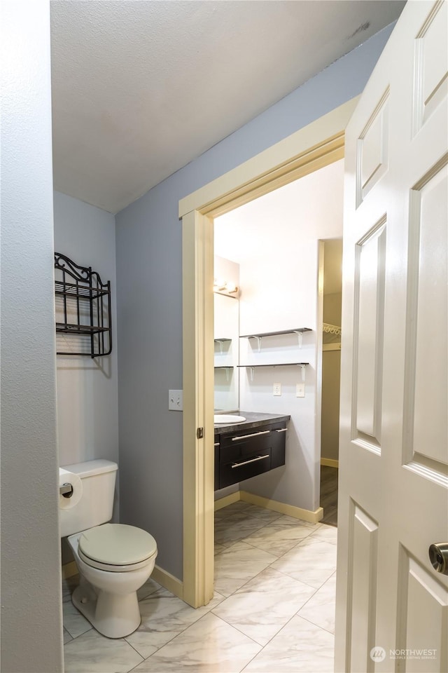 bathroom featuring marble finish floor, vanity, toilet, and baseboards