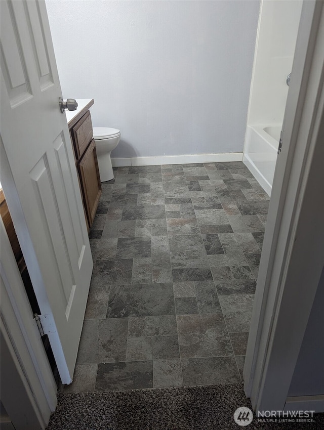 bathroom featuring a bathtub, toilet, vanity, and baseboards