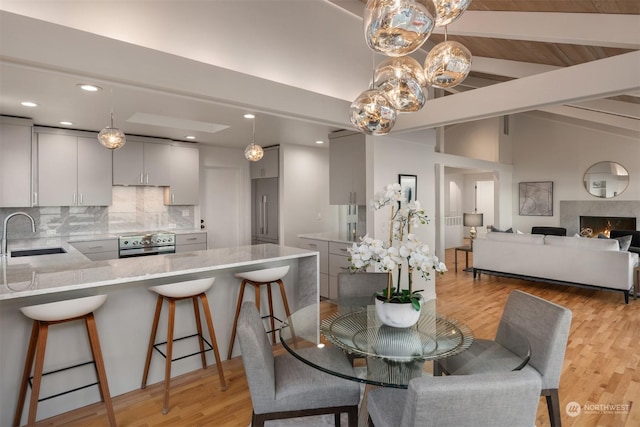 dining area featuring lofted ceiling with beams, sink, a fireplace, and light wood-type flooring